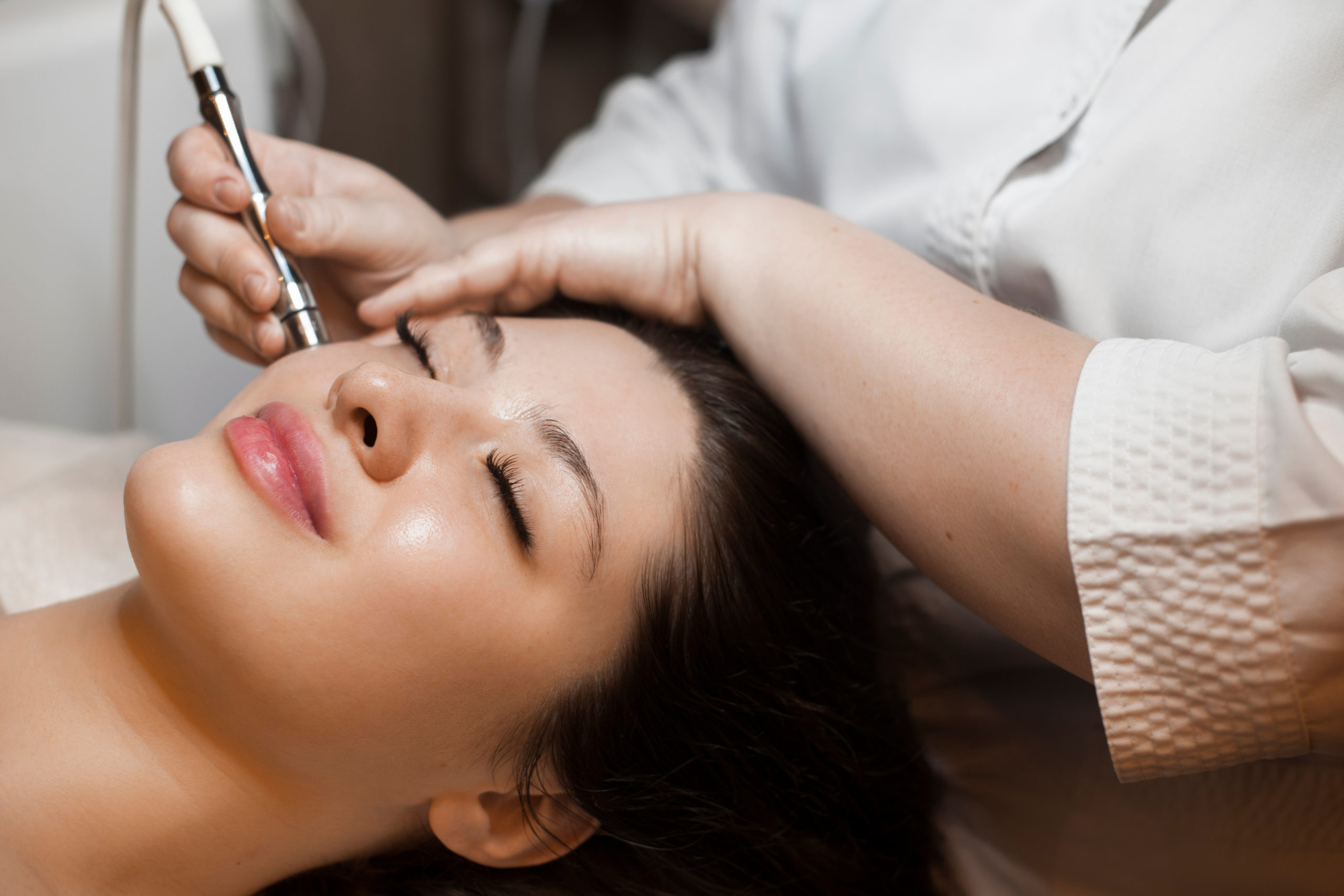 Close up side view portrait of a cute caucasian woman doing noninvasive microdermabrasion on her face with a dermapen by a cosmetician | Perfectly Made Aesthetic Boutique in Prosper, TX