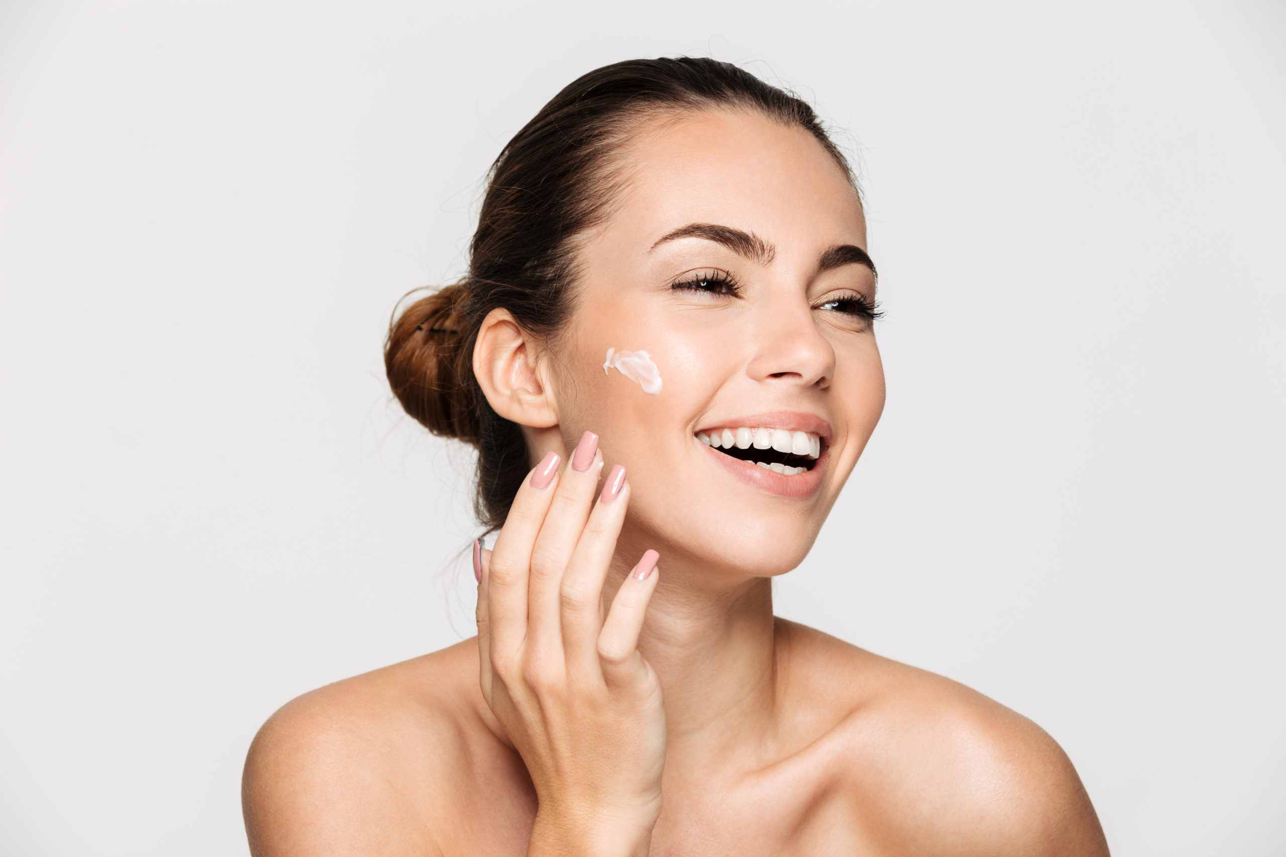 Close up beauty portrait of a laughing beautiful half naked woman applying face cream and looking away isolated over white background | Perfectly Made Aesthetic Boutique in Prosper, TX