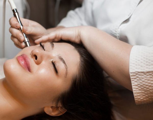 Close up side view portrait of a cute caucasian woman doing noninvasive microdermabrasion on her face with a dermapen by a cosmetician | Perfectly Made Aesthetic Boutique in Prosper, TX